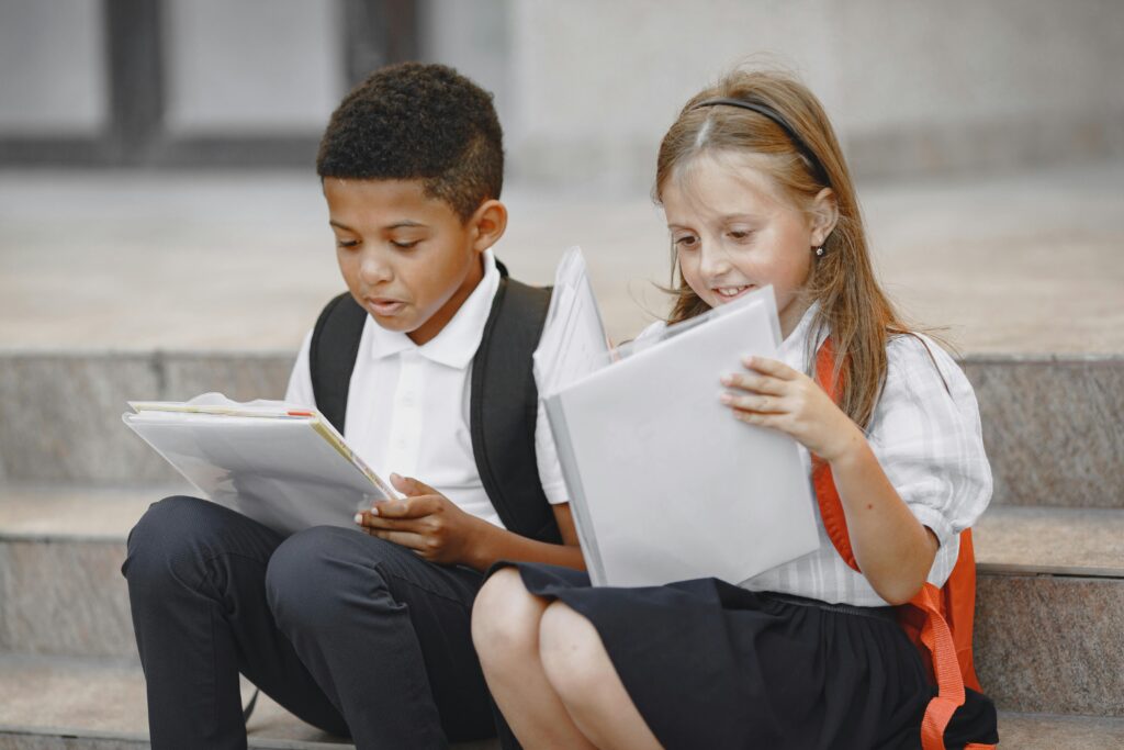 Two school-aged children sitting on steps, engrossed in reading books outdoors.